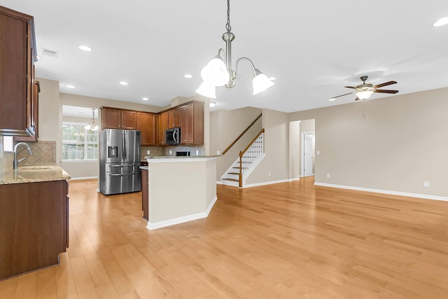 kitchen featuring a sink, open floor plan, appliances with stainless steel finishes, brown cabinets, and pendant lighting