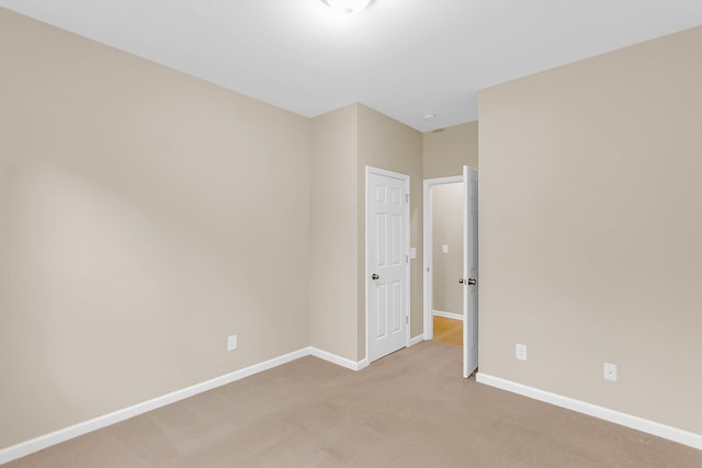 spare room featuring light colored carpet and baseboards