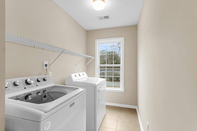 washroom featuring washing machine and clothes dryer, visible vents, light tile patterned flooring, laundry area, and baseboards