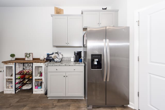 kitchen with light stone countertops, dark hardwood / wood-style flooring, stainless steel fridge, and white cabinets