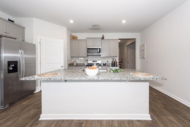 kitchen with a kitchen bar, appliances with stainless steel finishes, a kitchen island with sink, and dark wood-type flooring