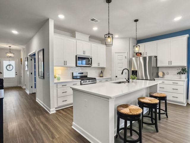 kitchen with white cabinetry, stainless steel appliances, hanging light fixtures, and a center island with sink