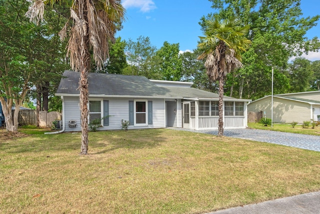 ranch-style home featuring driveway, a front lawn, fence, and a sunroom