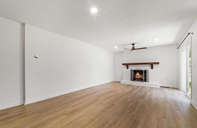 unfurnished living room with a fireplace, ceiling fan, plenty of natural light, and light hardwood / wood-style flooring