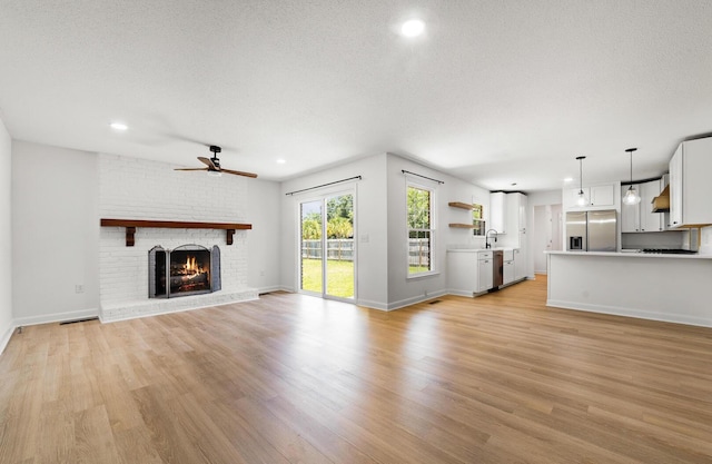 unfurnished living room featuring ceiling fan, sink, light hardwood / wood-style flooring, a textured ceiling, and a fireplace