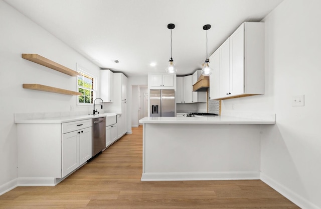 kitchen featuring white cabinets, custom range hood, appliances with stainless steel finishes, light hardwood / wood-style floors, and kitchen peninsula