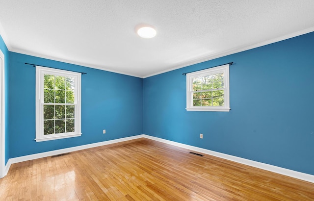 empty room featuring plenty of natural light, ornamental molding, a textured ceiling, and light wood-type flooring