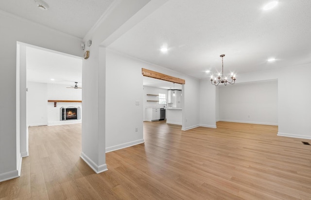 unfurnished living room with ceiling fan with notable chandelier, light hardwood / wood-style floors, a textured ceiling, and a brick fireplace