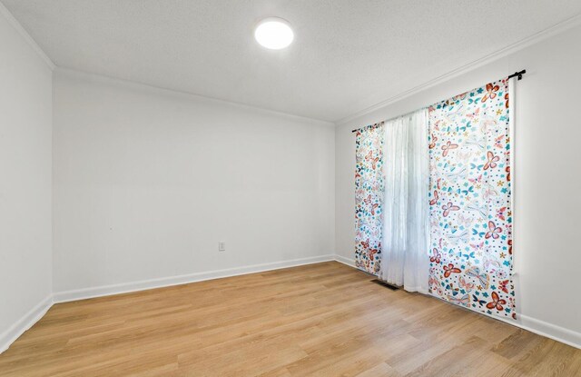 empty room with a textured ceiling, light wood-type flooring, and ornamental molding