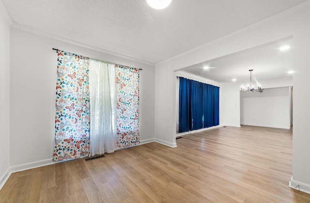 empty room featuring hardwood / wood-style floors, a notable chandelier, ornamental molding, and a textured ceiling