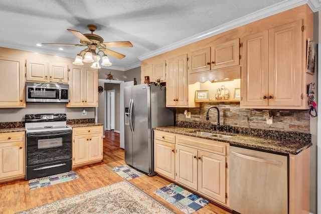 kitchen with sink, dark stone countertops, ornamental molding, stainless steel appliances, and light hardwood / wood-style flooring