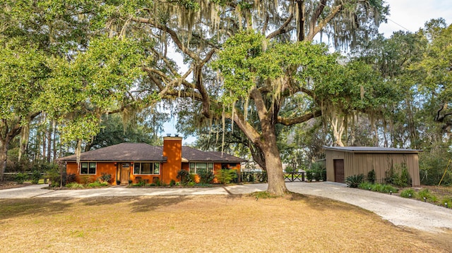 view of front of property with a front yard, a chimney, an outdoor structure, and driveway