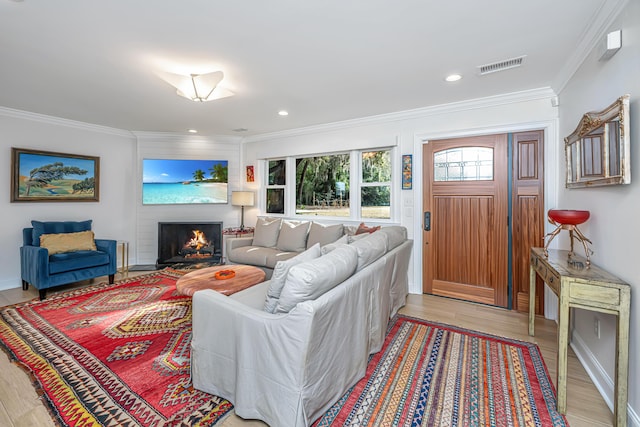 living room with a warm lit fireplace, visible vents, crown molding, light wood-style floors, and recessed lighting