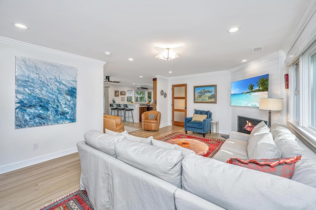 living area with a lit fireplace, baseboards, crown molding, and wood finished floors