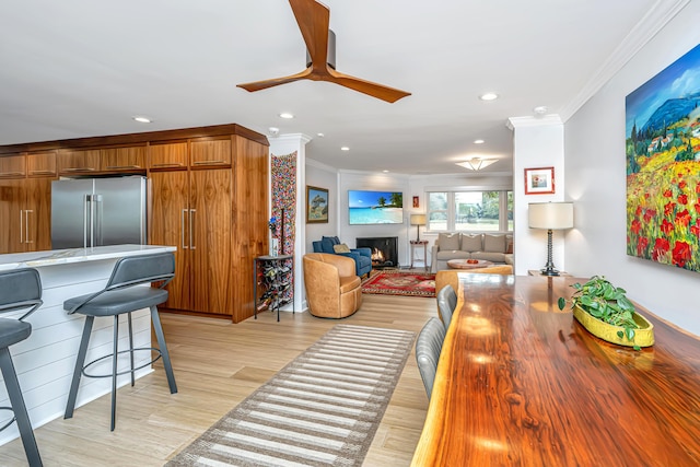 living room with light wood-style floors, a warm lit fireplace, crown molding, and recessed lighting