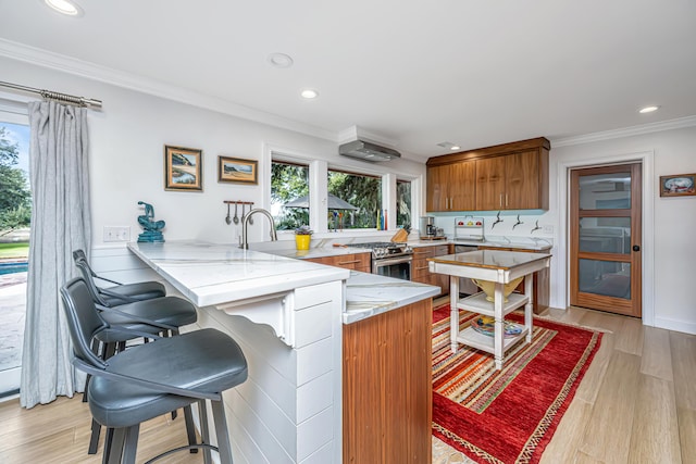 kitchen with light wood finished floors, brown cabinets, a peninsula, a kitchen bar, and stainless steel range with gas stovetop