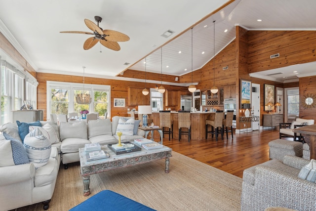 living area with visible vents, wood walls, wood finished floors, high vaulted ceiling, and a ceiling fan