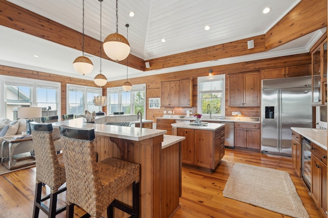 kitchen with stainless steel appliances, brown cabinetry, a large island with sink, and beverage cooler