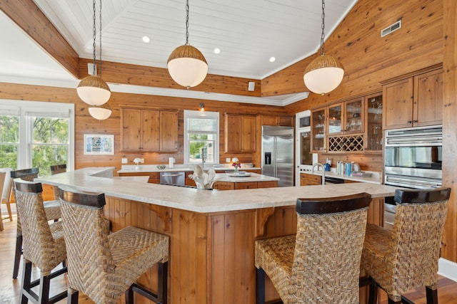 kitchen featuring wooden walls, appliances with stainless steel finishes, light countertops, a large island, and visible vents
