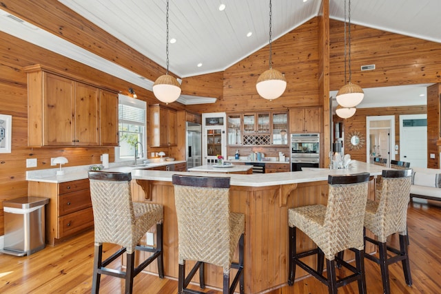 kitchen featuring wooden walls, brown cabinets, stainless steel appliances, and light wood-type flooring