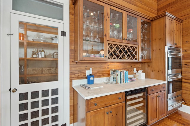 bar with stainless steel double oven, a dry bar, beverage cooler, wooden walls, and a warming drawer
