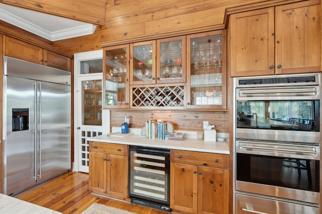 kitchen with wine cooler, wooden walls, light wood-type flooring, light countertops, and stainless steel appliances
