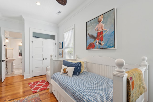bedroom with ensuite bathroom, visible vents, a sink, light wood-style floors, and ornamental molding