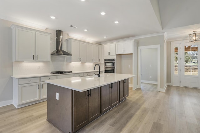 kitchen with a center island with sink, crown molding, sink, wall chimney exhaust hood, and appliances with stainless steel finishes