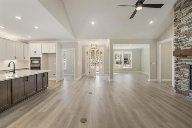 kitchen with ceiling fan with notable chandelier, light hardwood / wood-style flooring, white cabinets, a stone fireplace, and lofted ceiling