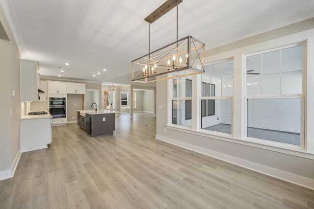 kitchen featuring appliances with stainless steel finishes, ceiling fan with notable chandelier, a kitchen island with sink, white cabinets, and hanging light fixtures