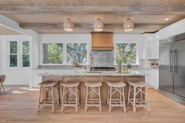 kitchen with white cabinets, stainless steel appliances, premium range hood, and a center island with sink