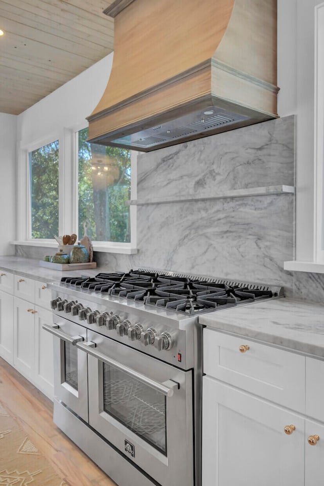 kitchen with light stone countertops, premium range hood, double oven range, light hardwood / wood-style flooring, and white cabinets