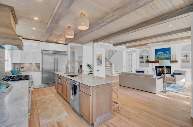 kitchen with white cabinetry, sink, light stone countertops, premium appliances, and a kitchen island with sink