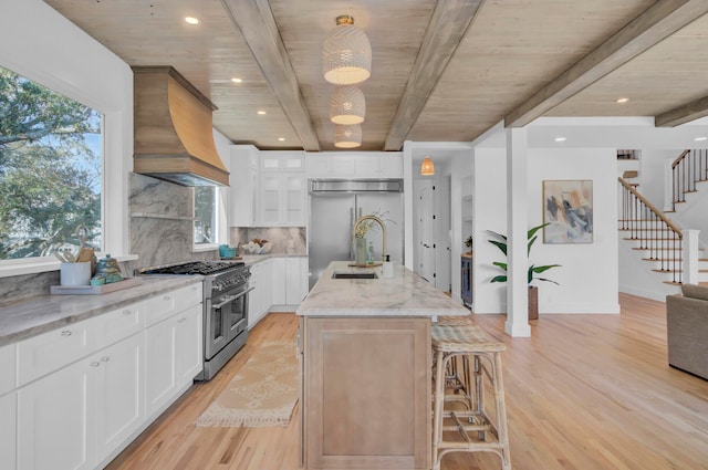 kitchen with white cabinetry, custom exhaust hood, high quality appliances, and an island with sink