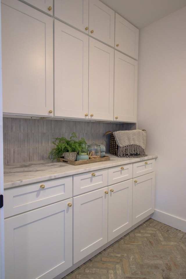 kitchen with tasteful backsplash, light stone countertops, and white cabinets