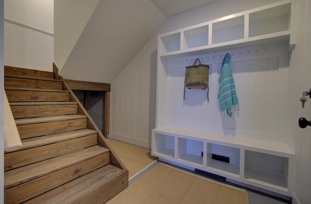 mudroom with light colored carpet, vaulted ceiling, and wooden walls