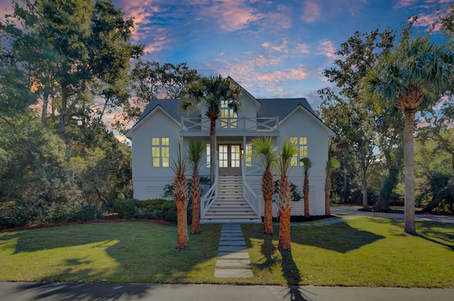 view of front of home featuring french doors, a balcony, a porch, and a lawn