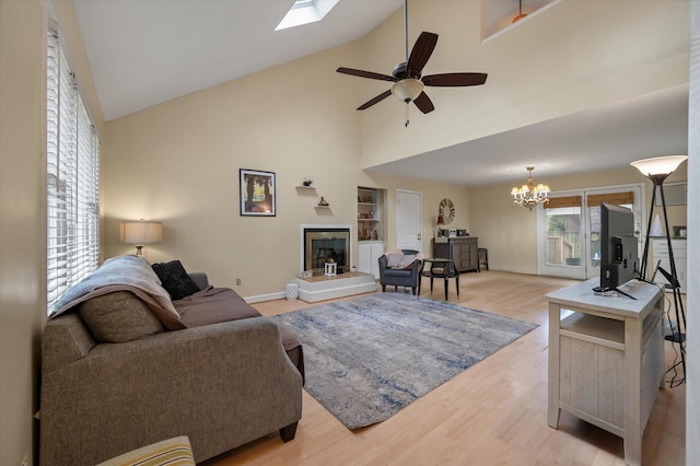 living room featuring ceiling fan with notable chandelier, a skylight, high vaulted ceiling, and light hardwood / wood-style flooring