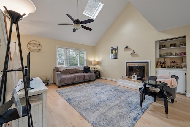 living room with high vaulted ceiling, a skylight, light hardwood / wood-style floors, and ceiling fan