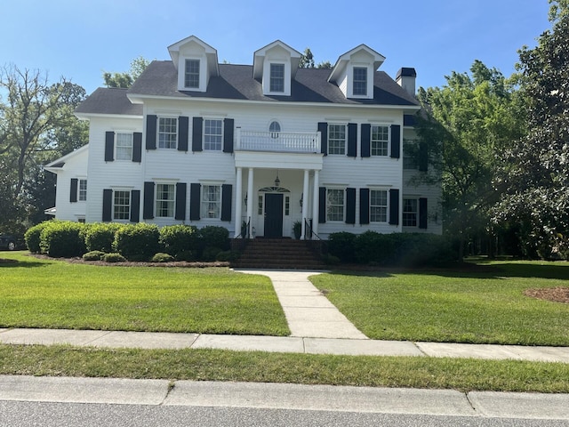 view of front facade featuring a chimney, a front yard, and a balcony