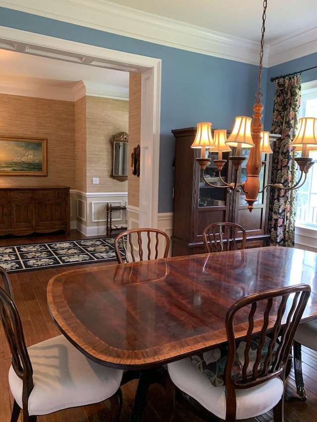 dining area with a decorative wall, a chandelier, crown molding, wainscoting, and wood finished floors
