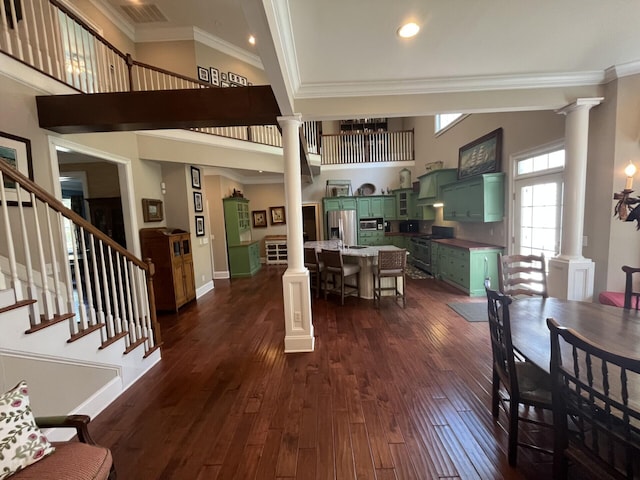 dining area featuring a high ceiling, crown molding, dark wood-style floors, and ornate columns