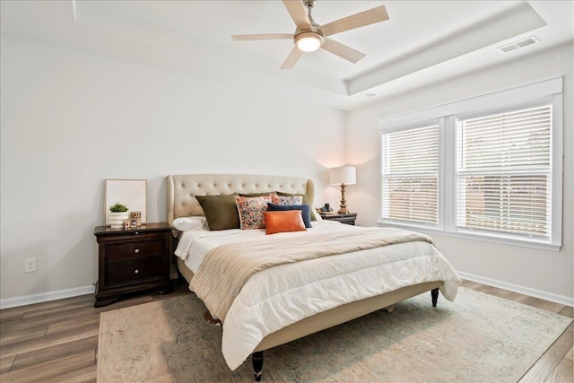 bedroom with ceiling fan, dark wood-type flooring, and a tray ceiling