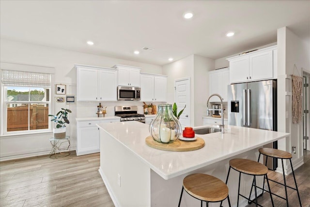 kitchen featuring a kitchen breakfast bar, appliances with stainless steel finishes, white cabinets, and a kitchen island with sink