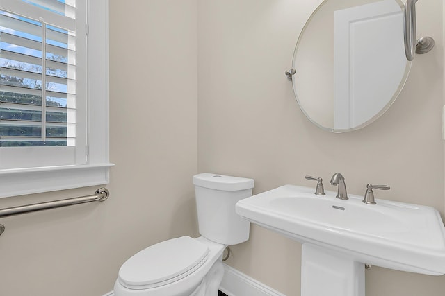 half bathroom with toilet, baseboards, and a sink