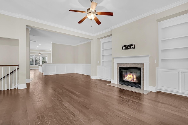 unfurnished living room with a ceiling fan, built in features, a glass covered fireplace, wood finished floors, and crown molding