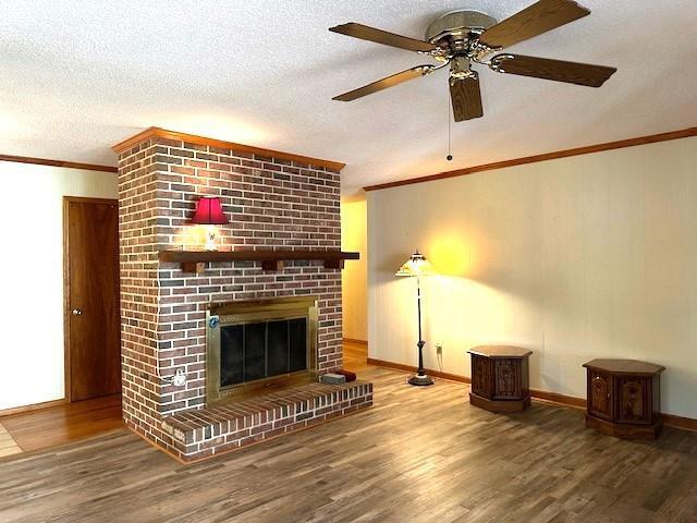 unfurnished living room featuring a brick fireplace, wood-type flooring, a textured ceiling, and ceiling fan