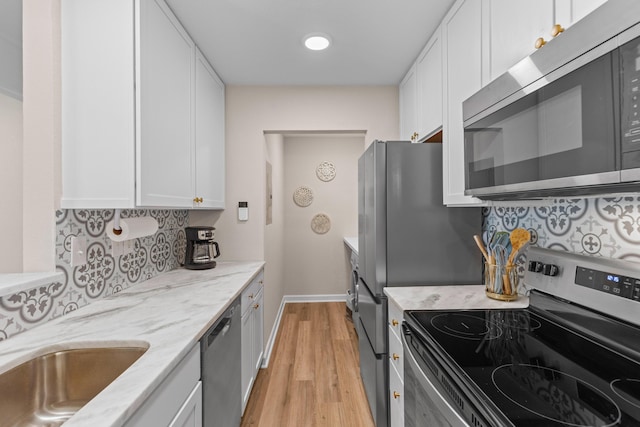 kitchen featuring light wood-style flooring, white cabinets, appliances with stainless steel finishes, light stone countertops, and tasteful backsplash