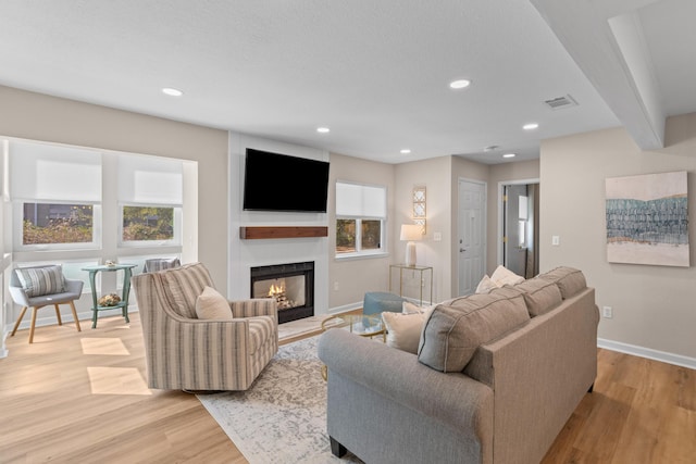 living room with light wood-type flooring, a glass covered fireplace, visible vents, and baseboards