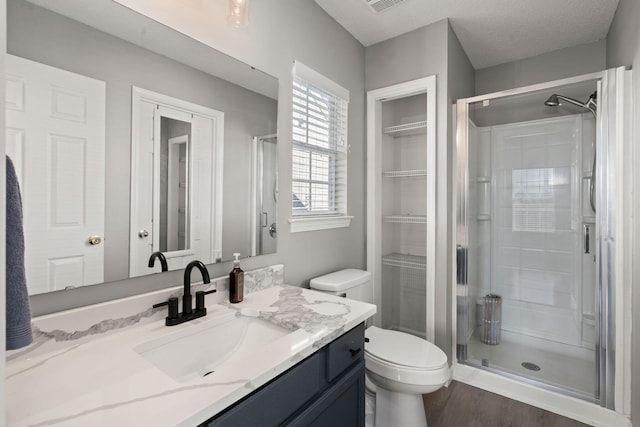 bathroom featuring a stall shower, visible vents, toilet, wood finished floors, and vanity